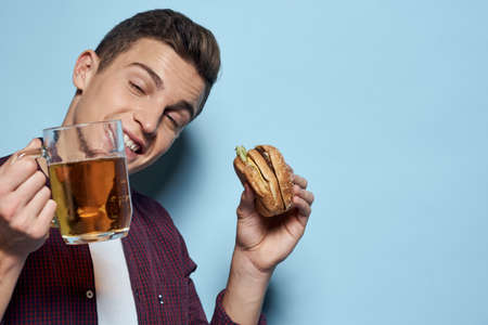cheerful drunk man with beer mug and hamburger in hand diet food lifestyle blue backgroundの写真素材