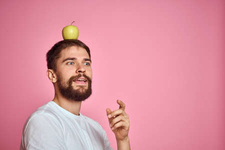 Cute man with an apple on a pink background gestures with his hands cropped white T-shirt Copy Spaceの写真素材