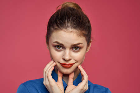 energetic woman with bright makeup and in a blue shirt on a pink background gestures with her hands