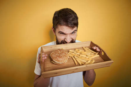 Man with wooden pallet fast food hamburger french fries diet food intake close-upの写真素材