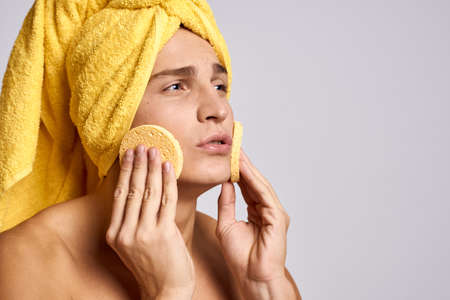 Handsome man with cosmetology facial sponge and yellow towel on his headの写真素材