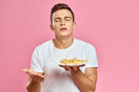 Man with French fries in a paper box on a pink background calories fast food portrait pink...