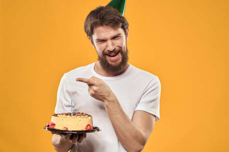 Handsome man with a beard and in a cap celebrating a birthday party yellow backgroundの写真素材
