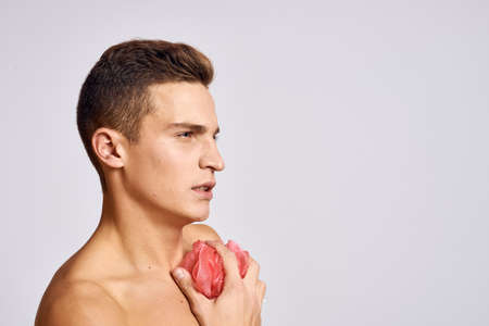 naked guy with a pink sponge in his hand washes his body on a light background cropped view