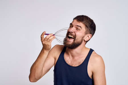 man with a massager for the head and in a blue t-shirt on a light background relaxing beard emotionsの写真素材