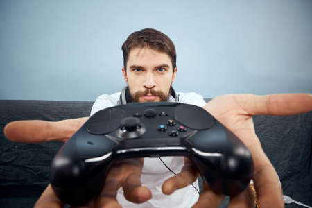 A man sits on a sofa with a gamepad in his hand. Leisure lifestyle game console