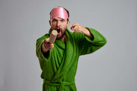 man with rolling pin in hand green robe pink sleep mask cropped view