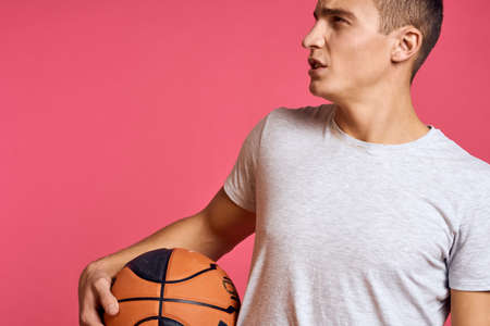 Guy with a basketball ball on a pink background in a white t-shirt cropped view Sport model workout