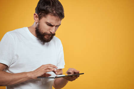 Man with a tablet on a yellow background in a white t-shirt new technologies businessman touch screen touchpadの写真素材