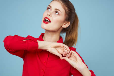 A girl in bright clothes shows a heart with her hands on a blue background cropped view