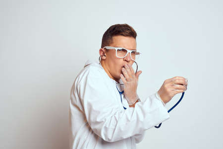doctor in a medical gown with a stethoscope and glasses on a light background cropped view portraitの写真素材
