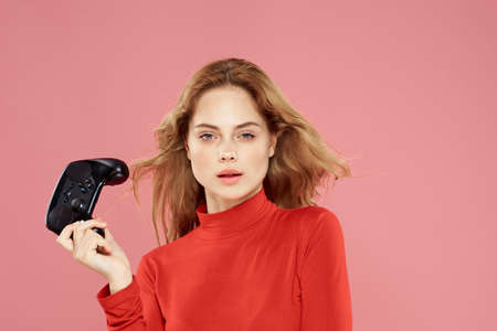 Woman with gamepad in hand entertainment video games lifestyle technology red blouse pink background