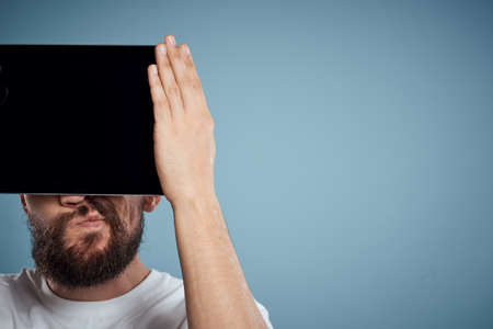 man with touch tablet in front of face on blue background cropped view copy space emotions model