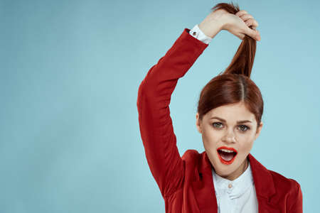 Woman holds hair with hands red jacket cosmetics close-up blue background