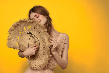 Woman in a straw hat in her hands on a yellow background emotions cropped view