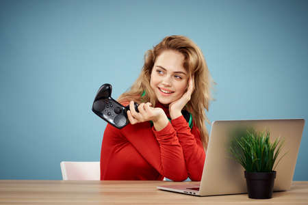Woman sitting at a table in front of a laptop headphones controller playing online lifestyle blue...