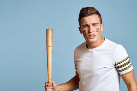 baseball guy with a bat in his hand on a blue background and a combat color on his face makeup model...