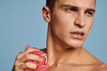 Young guy with a pink washcloth in his hand on a blue background skin care dermatology model cropped viewの写真素材