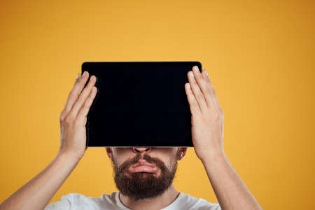Portrait of a man with a tablet in front of his face on a yellow background cropped view of a white...