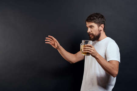 Man with a mug of beer in his hands emotions fun lifestyle white t-shirt dark isolated background