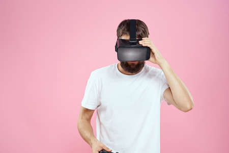 Man in virtual reality glasses joystick playing video lifestyle white t-shirt pink background