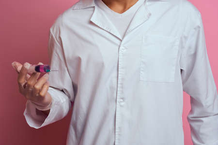 A doctor in a medical mask and gloves holds a syringe in the hands of an injection laboratory
