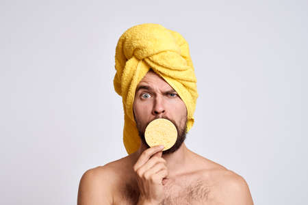 man with a yellow towel on his head bare shoulders sponge clean skin facial care light backgroundの写真素材