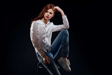 pretty woman sitting on a chair posing white shirt jeans long hair red lips dark background