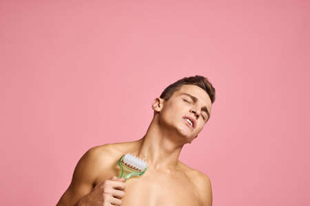 Handsome man with massager in hand on isolated pink background cropped view clean skinの写真素材