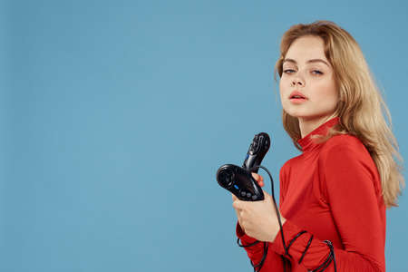 Woman holding in her hands two game controllers entertainment lifestyle red jacket blue background