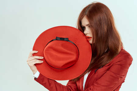 Elegant woman in red jacket hat holding long hair cropped light backgroundの写真素材