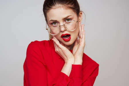 fashionable woman in a red shirt on a light background fun emotions bright makeup glasses attractive appearanceの写真素材
