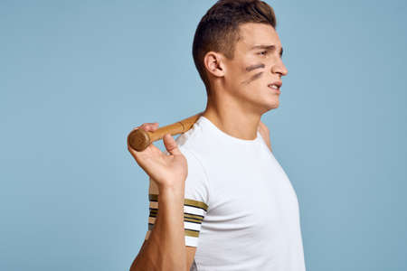 baseball guy with a bat in his hand on a blue background and a combat color on his face makeup model...