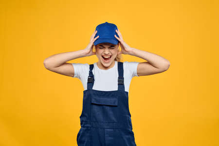 Woman in working uniform blue cap delivering courier service yellow backgroundの写真素材