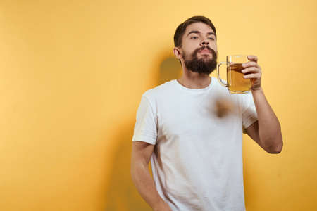 Man with a mug of beer fun alcohol lifestyle white t-shirt yellow isolated backgroundの写真素材