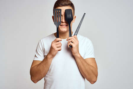 Guy with kitchen tools in hands on a light background cropped view of emotions fun modelの写真素材