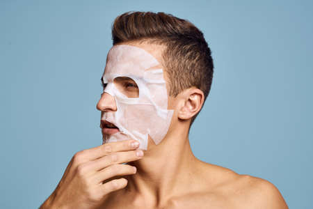 Nude man with white nourishing mask on face on blue background cropped viewの写真素材