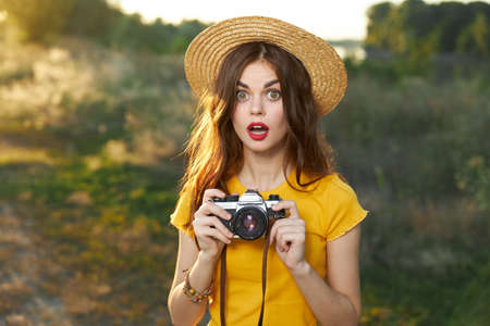 Enamored woman holding a camera in her hands hat red lips yellow t-shirt fresh airの写真素材