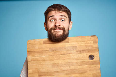 cute man with kitchen board near face on blue backgroundの写真素材