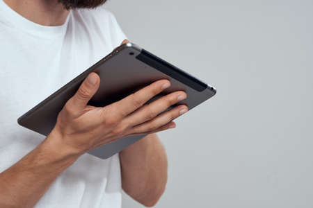 Tablet with a touch screen on a light background male hands white t-shirt cropped view