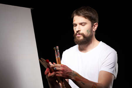 A man with a palette in his hands brush easel art Creative approach hobby dark background