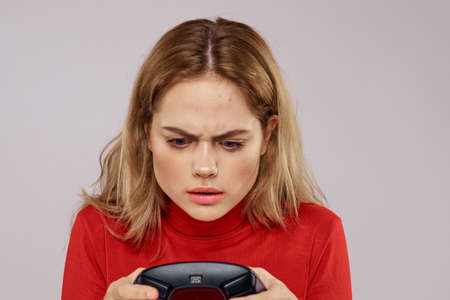 Woman with gamepad in hands playing games emotions lifestyle leisure red shirt light backgroundの写真素材