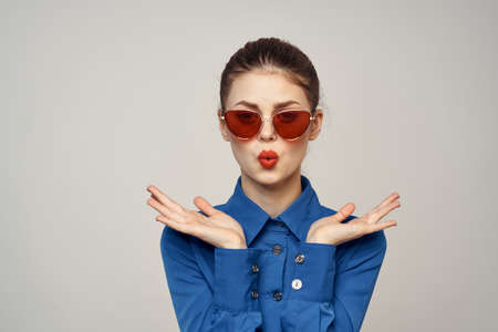 Fashionable woman in sunglasses and a blue shirt gesturing with her hands on a light background cropped viewの写真素材