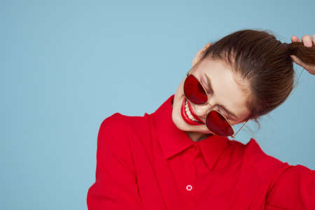 Woman in red shirt on blue background holds hands near face and sunglasses red lips makeup modelの写真素材
