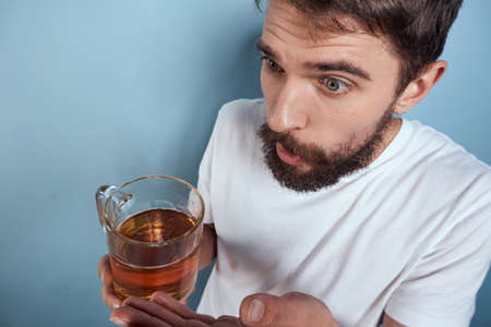 Cheerful man in a white T-shirt with a beer mug drunk blue background