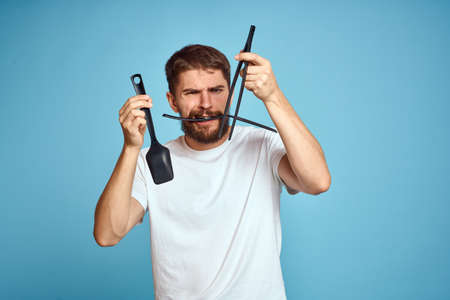 Bearded man with tools for cooking on a blue background and a white T-shirt shovelの写真素材