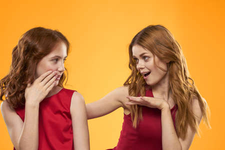 A red-haired girl and a beautiful woman on a yellow background in red dresses gesticulate with their...