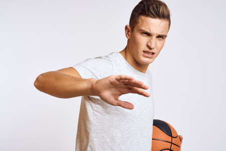 happy man with ball in hand and in white t-shirt on light background gesturing with hands cropped...