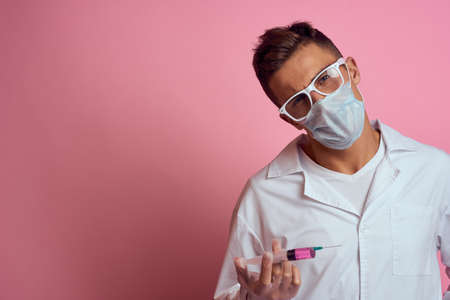 A doctor in a medical mask and gloves holds a syringe in the hands of an injection laboratory