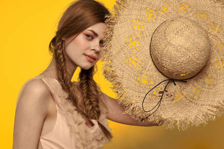Woman in a straw hat in her hands on a yellow background emotions cropped view